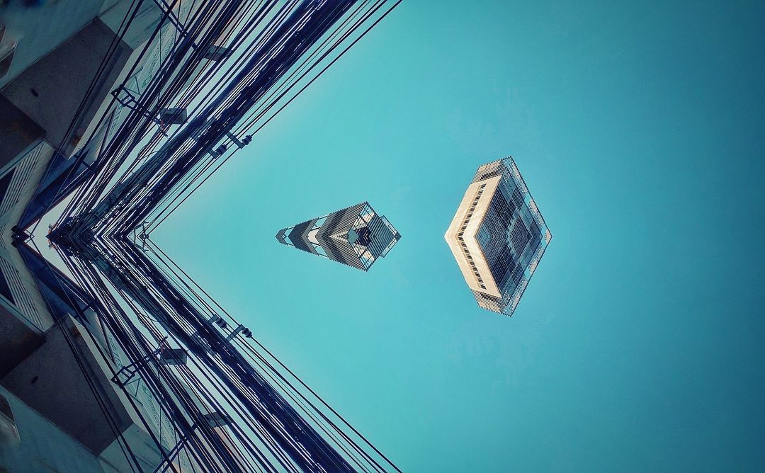 Upward view of city buildings with power lines against blue sky